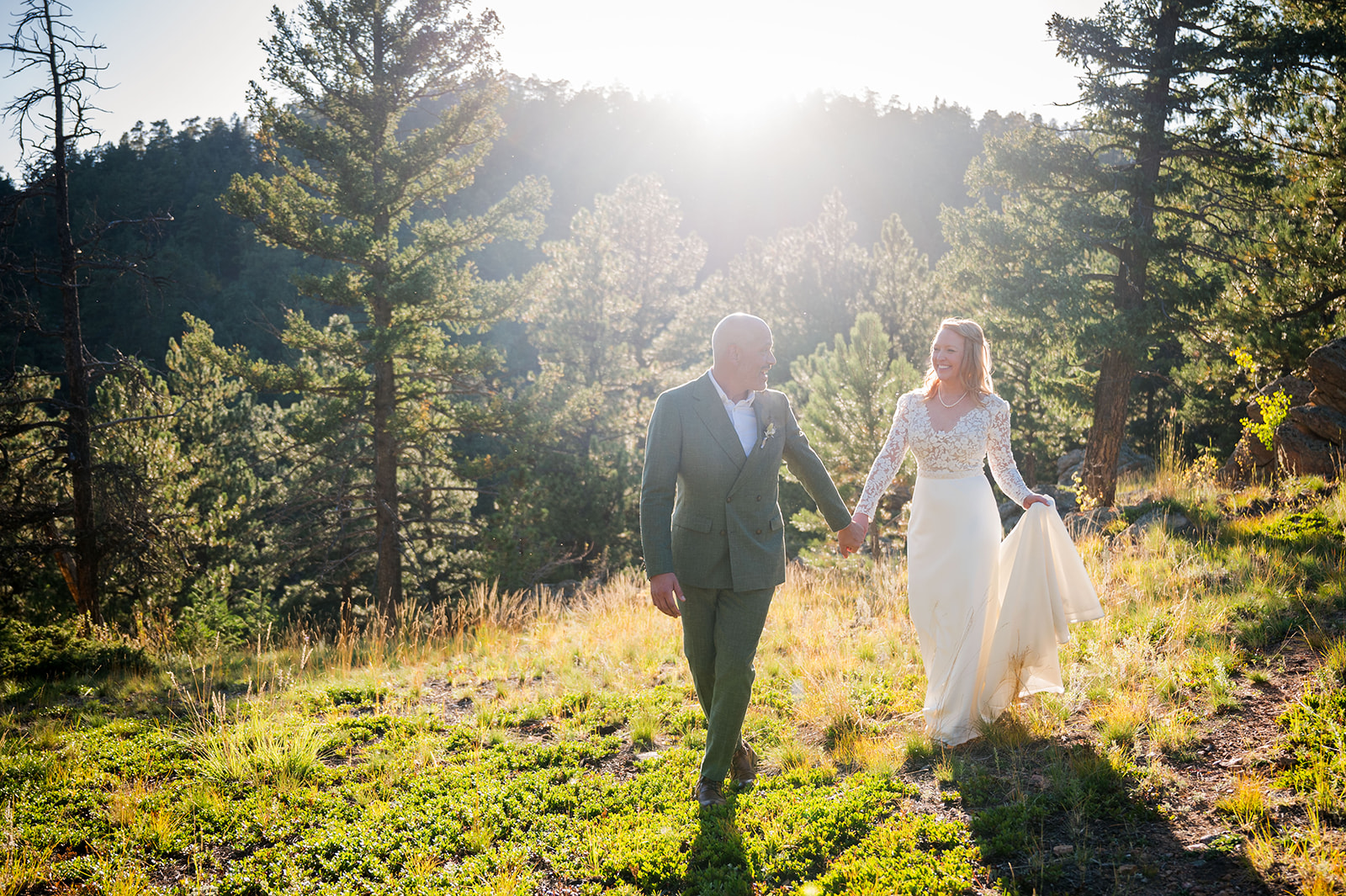 The bride and groom walk hand-in-hand toward the camera with the sun setting behind them.