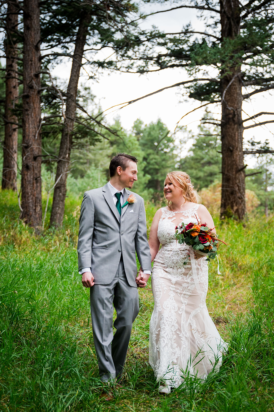 A bride and groom walk casually toward the camera holding hands and smiling at one another.