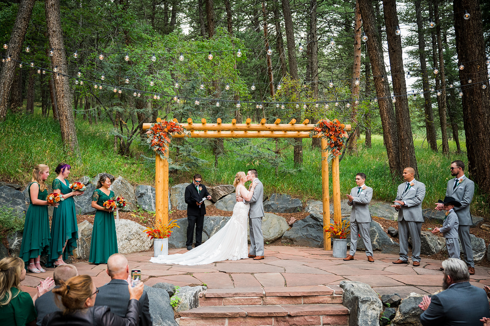 A couple sharing their first kiss under a wedding arbor at The Pines by Wedgewood Weddings in Genesee, Colorado.