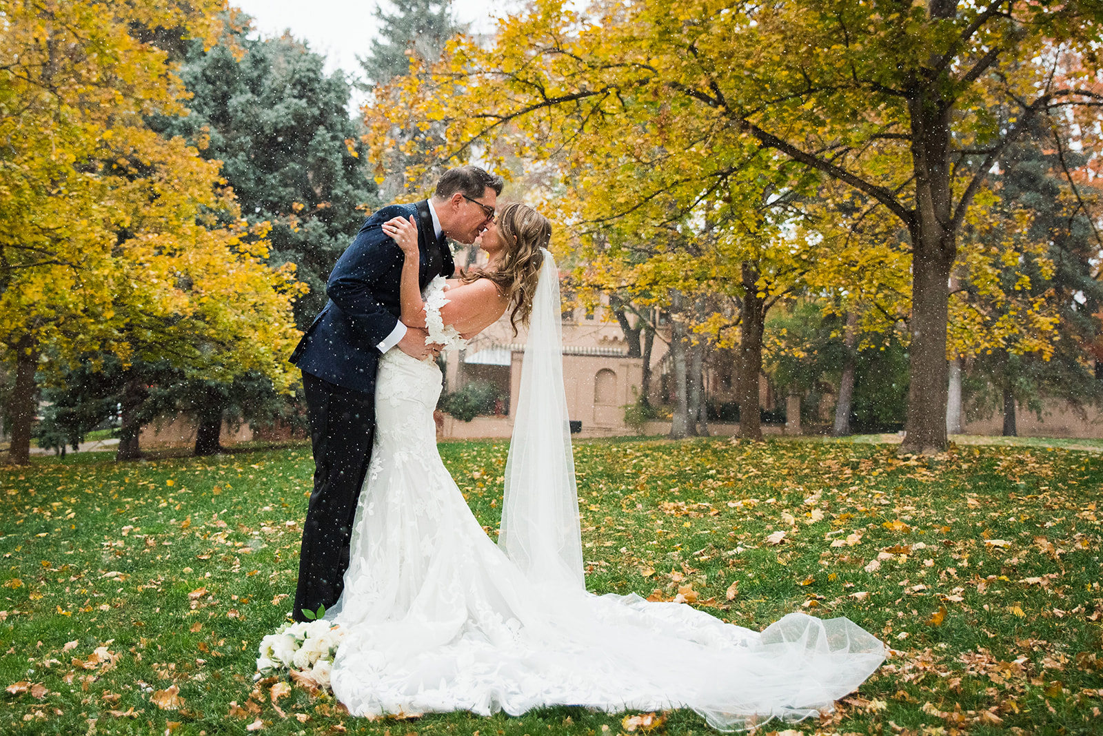 A groom dips his bride for a kiss with the yellow fall leaves in the background.