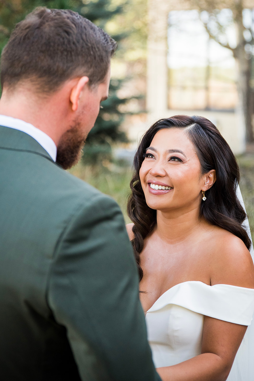 A bride smiles up at her groom as he reads his vows during their first look.