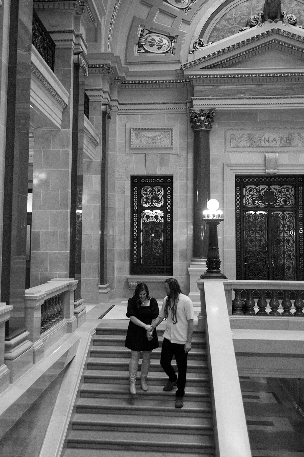 an engaged couple walks down the steps in the Wisconsin State Capitol building in Madison