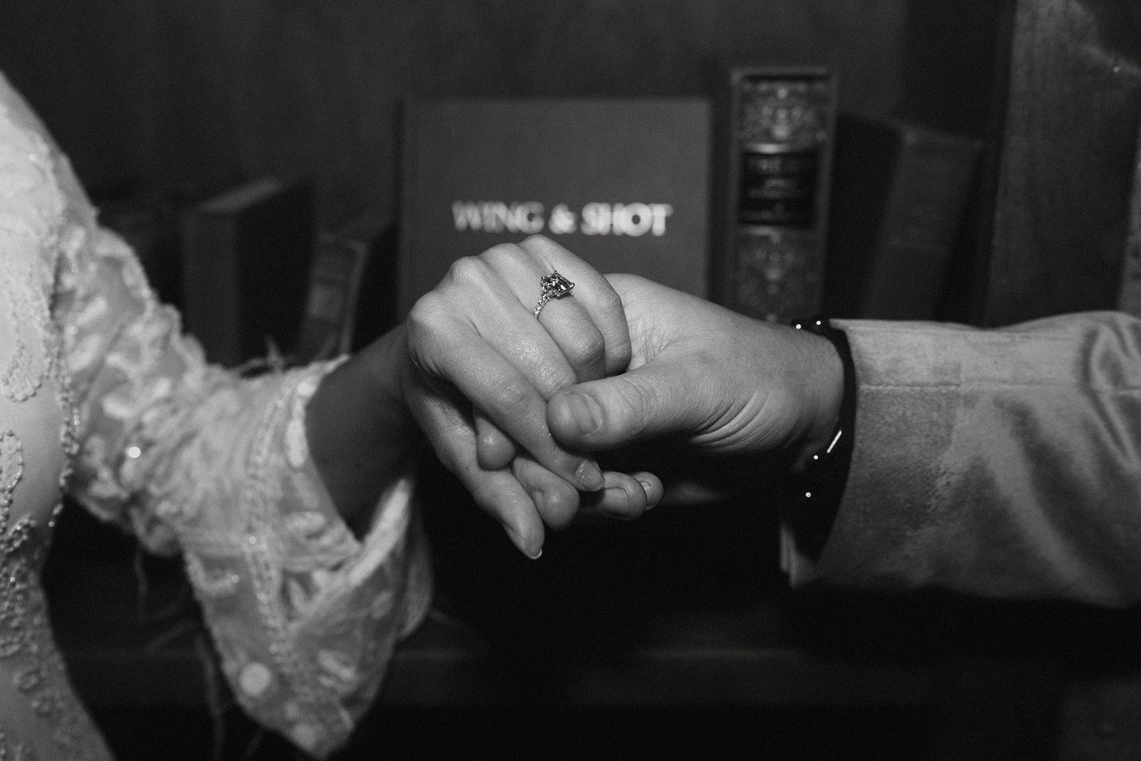 Black and white image of a man and woman holding hands showing off the engagement ring 
