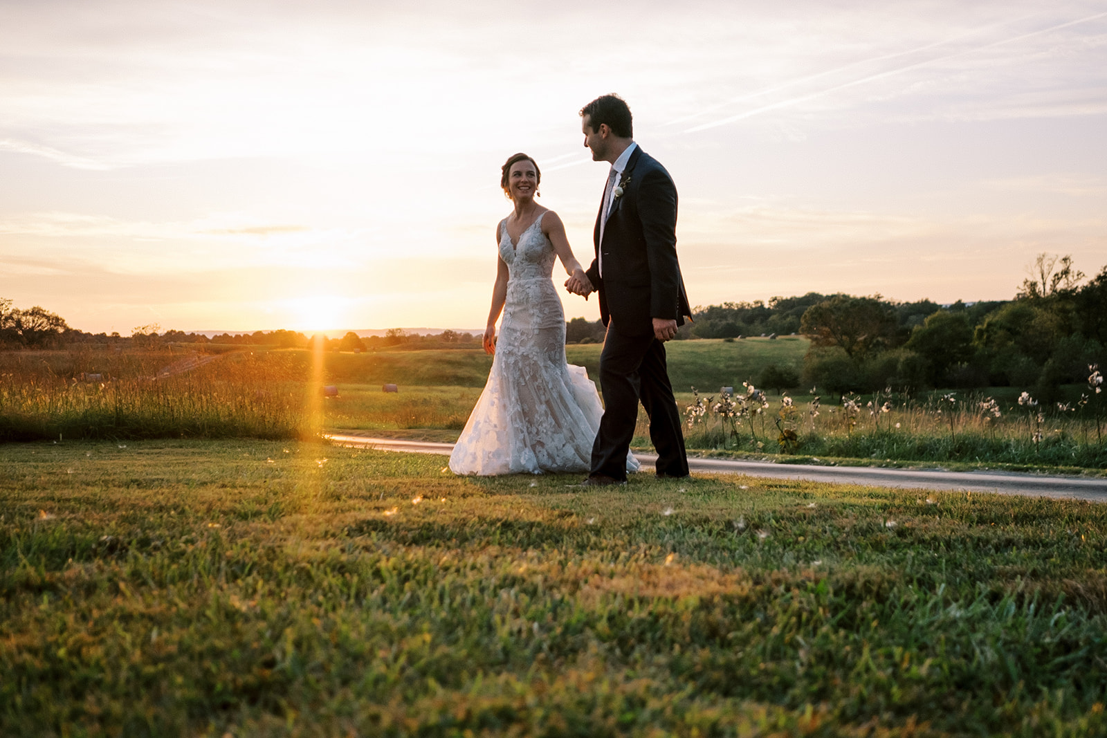 Bride and groom walking through the fields at sunset at Goodstone wedding