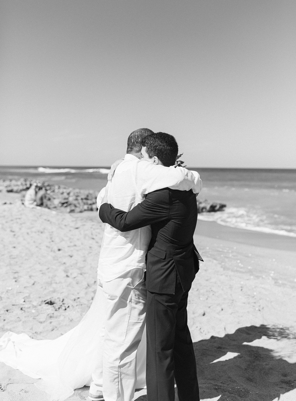 Groom hugs father of the bride after walk down the aisle at beach wedding in Palm Beach, Florida