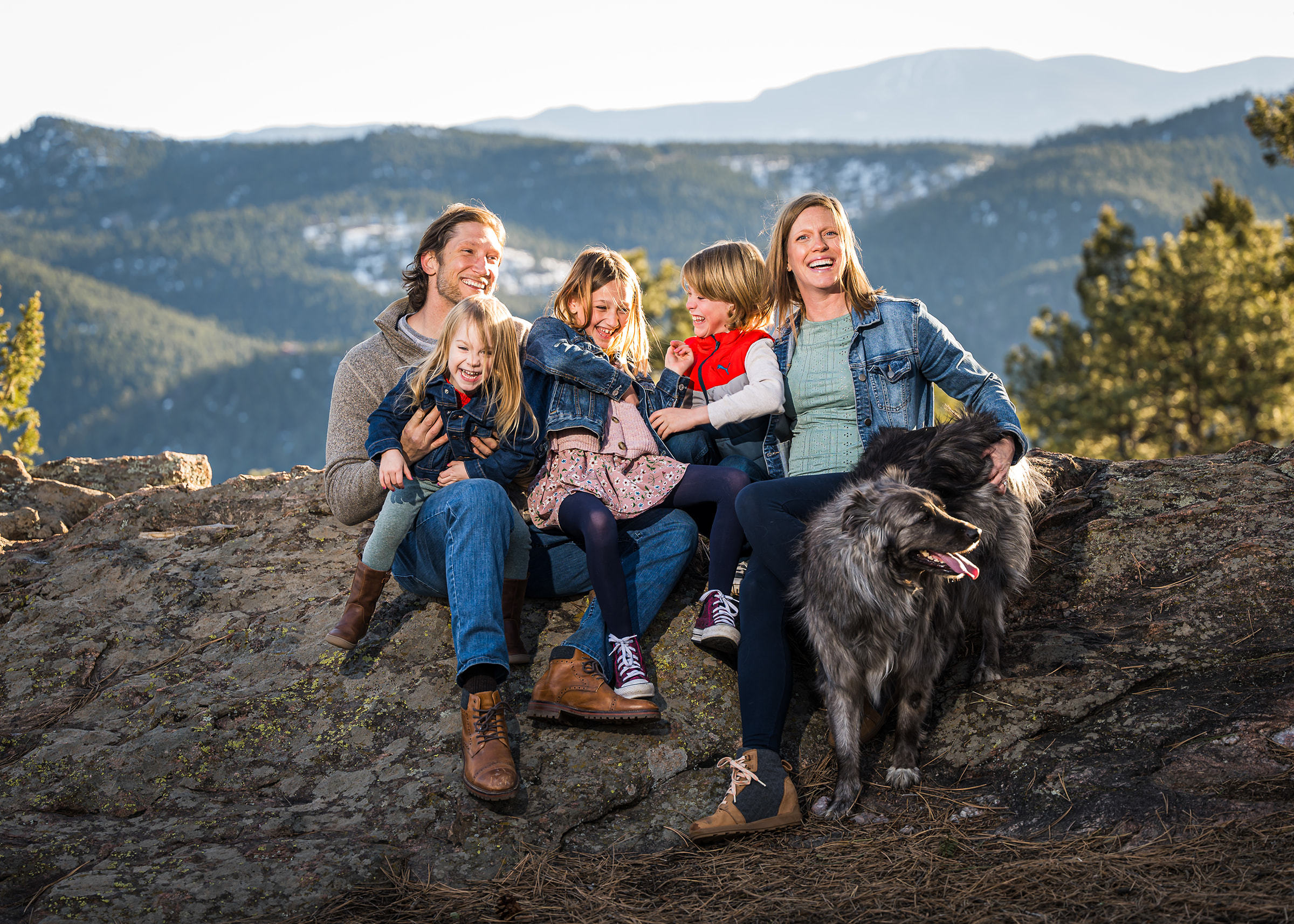 family portraits sitting on rock with mountains and trees tickling and laughing denver colorado photography