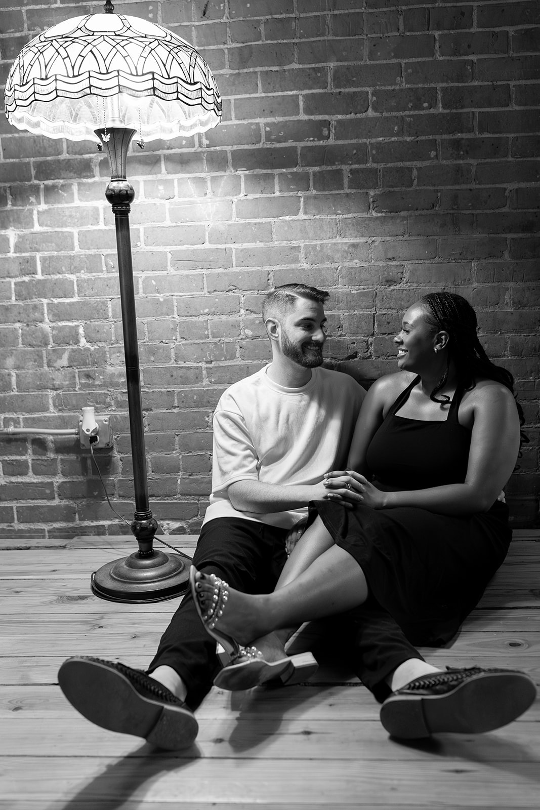couple sitting in front of brick wall with tiffany lamp during engagement session