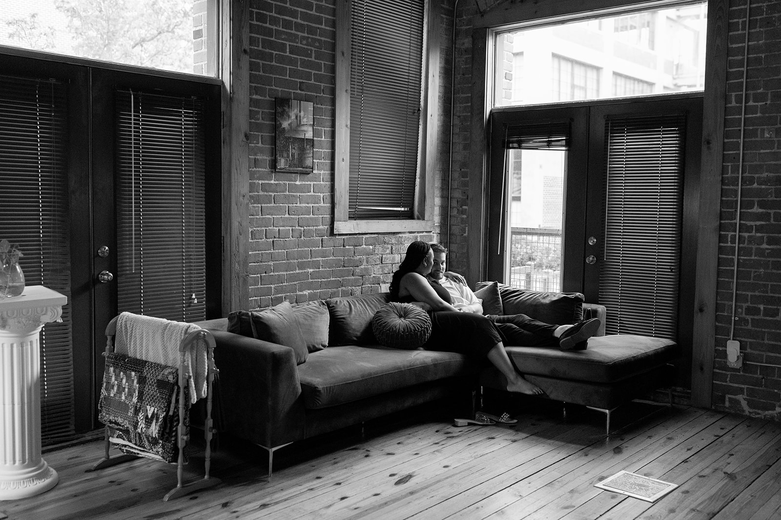 couple sitting on their couch with brick wall in apartment during engagement session
